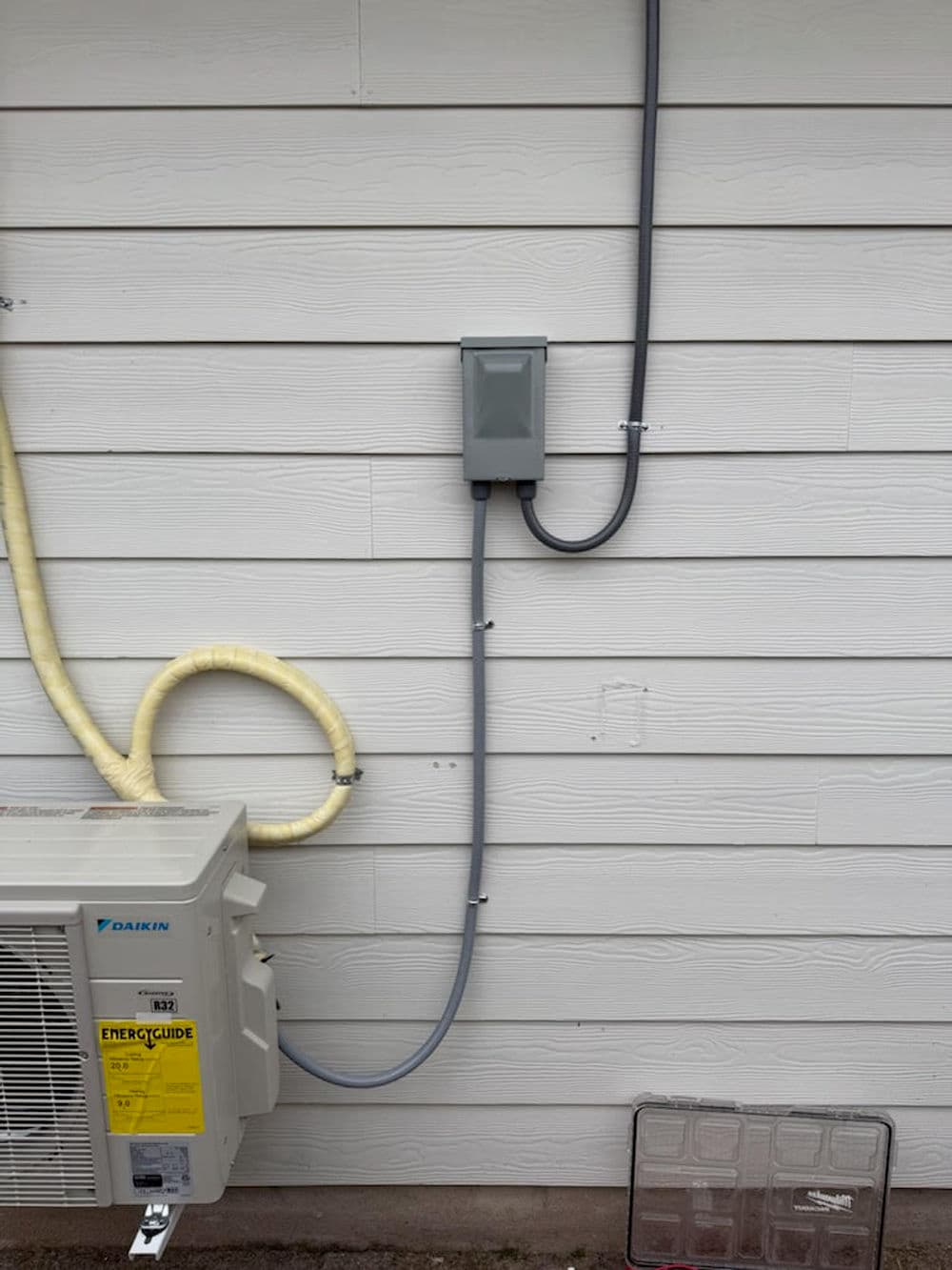 Daikin air conditioning unit connected to wall electrical box and conduit on exterior.