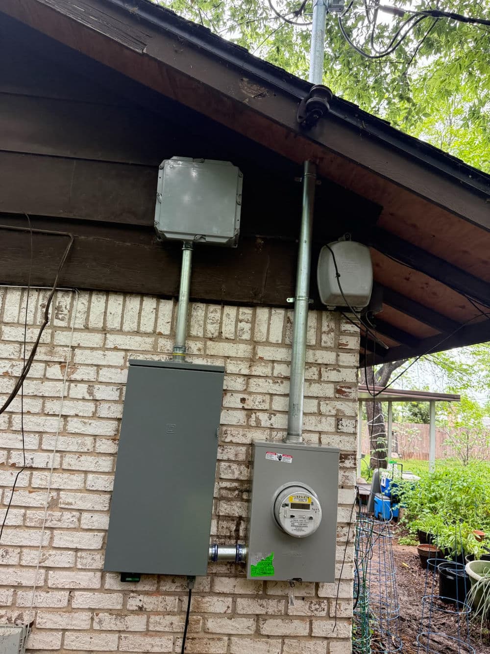 Electrical service panel and smart meter installed on a brick wall under a roof eave.