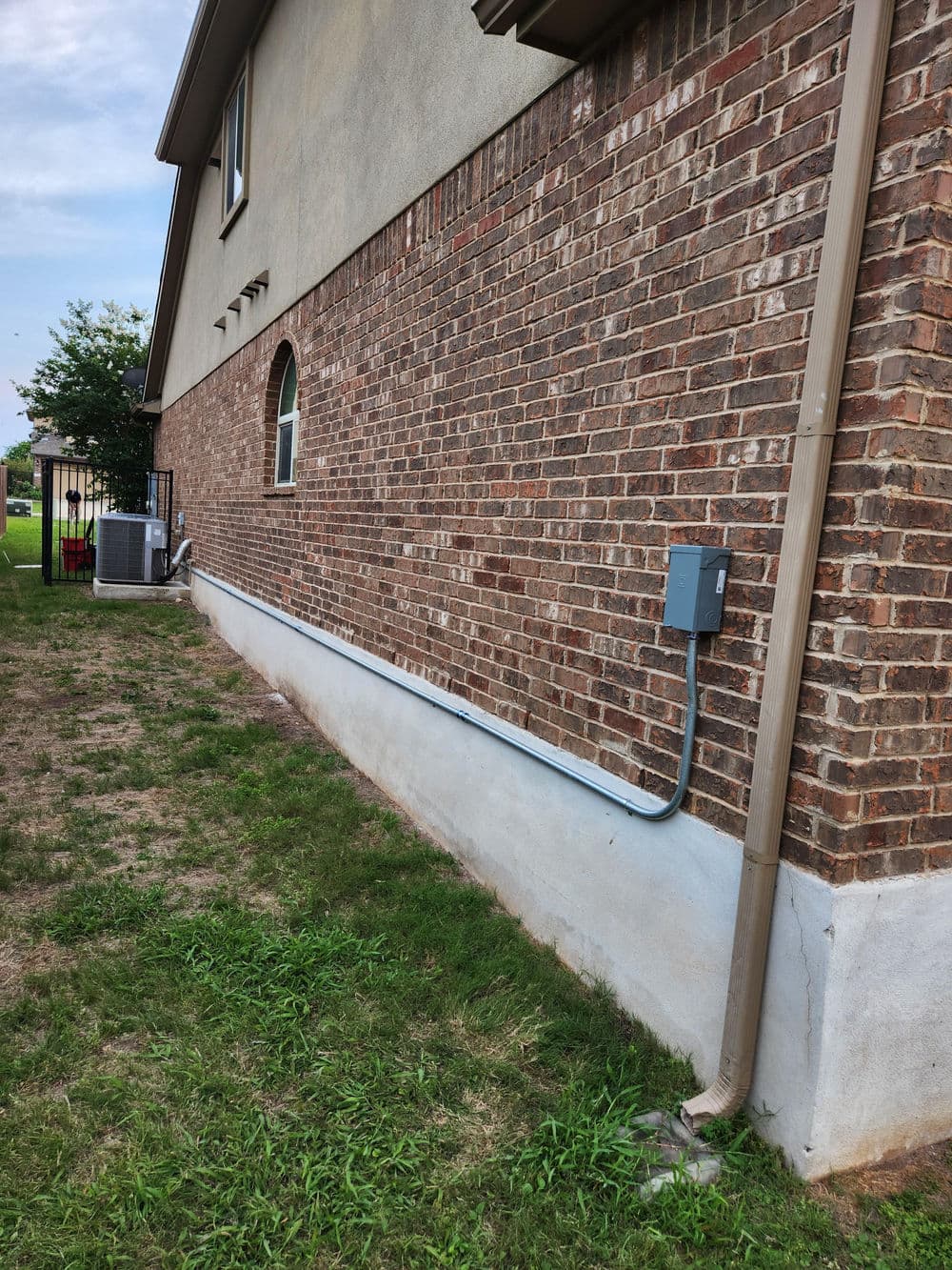 Exterior view of a brick wall with electrical panel and conduit, grass area beside house.