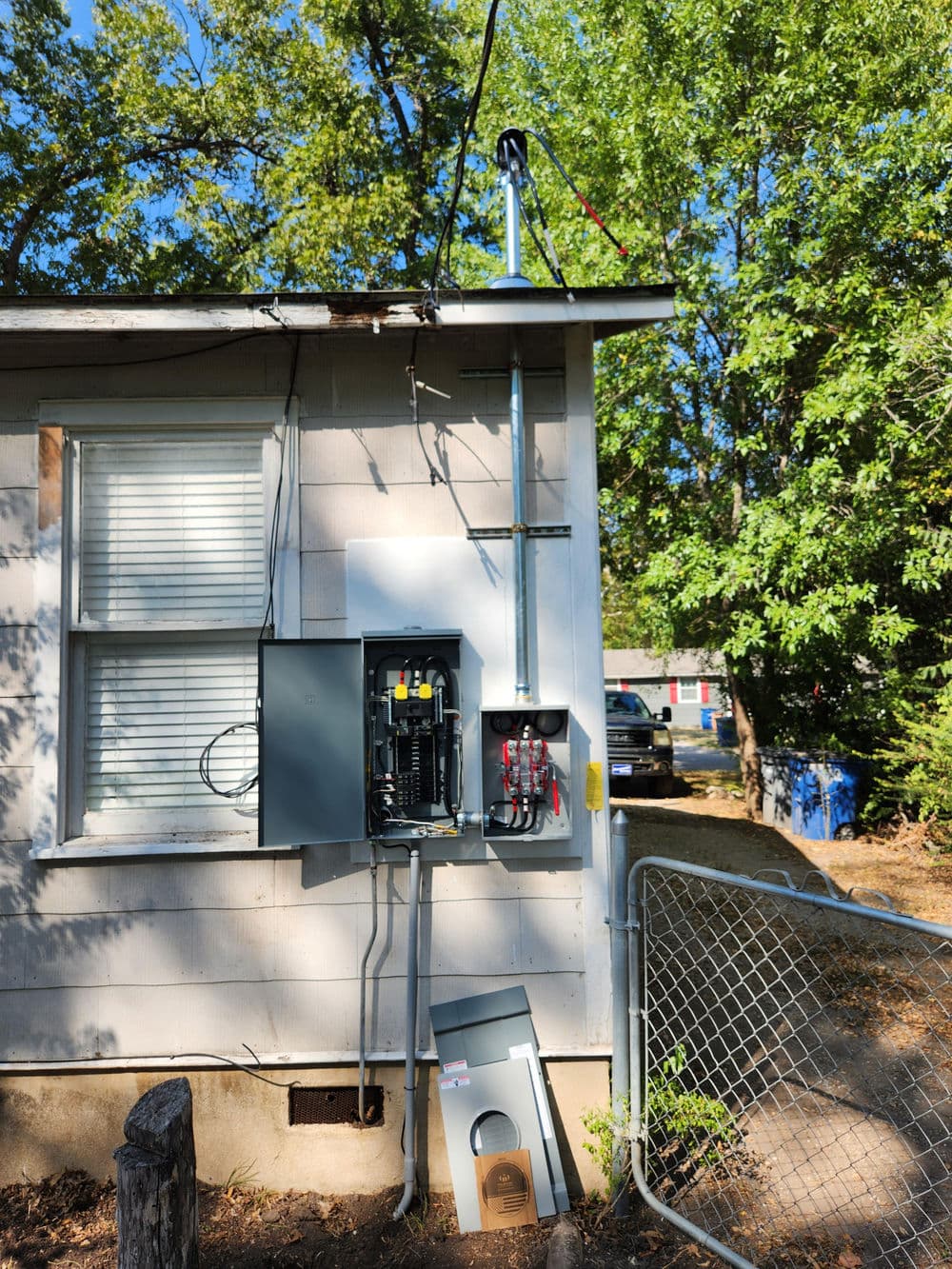 Electrical panel installation on a residential home with a nearby antenna and fence.