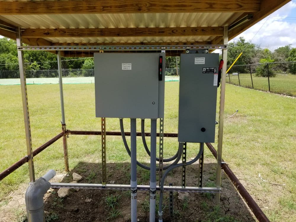 Electrical control boxes installed in a metal enclosure on a grassy field.