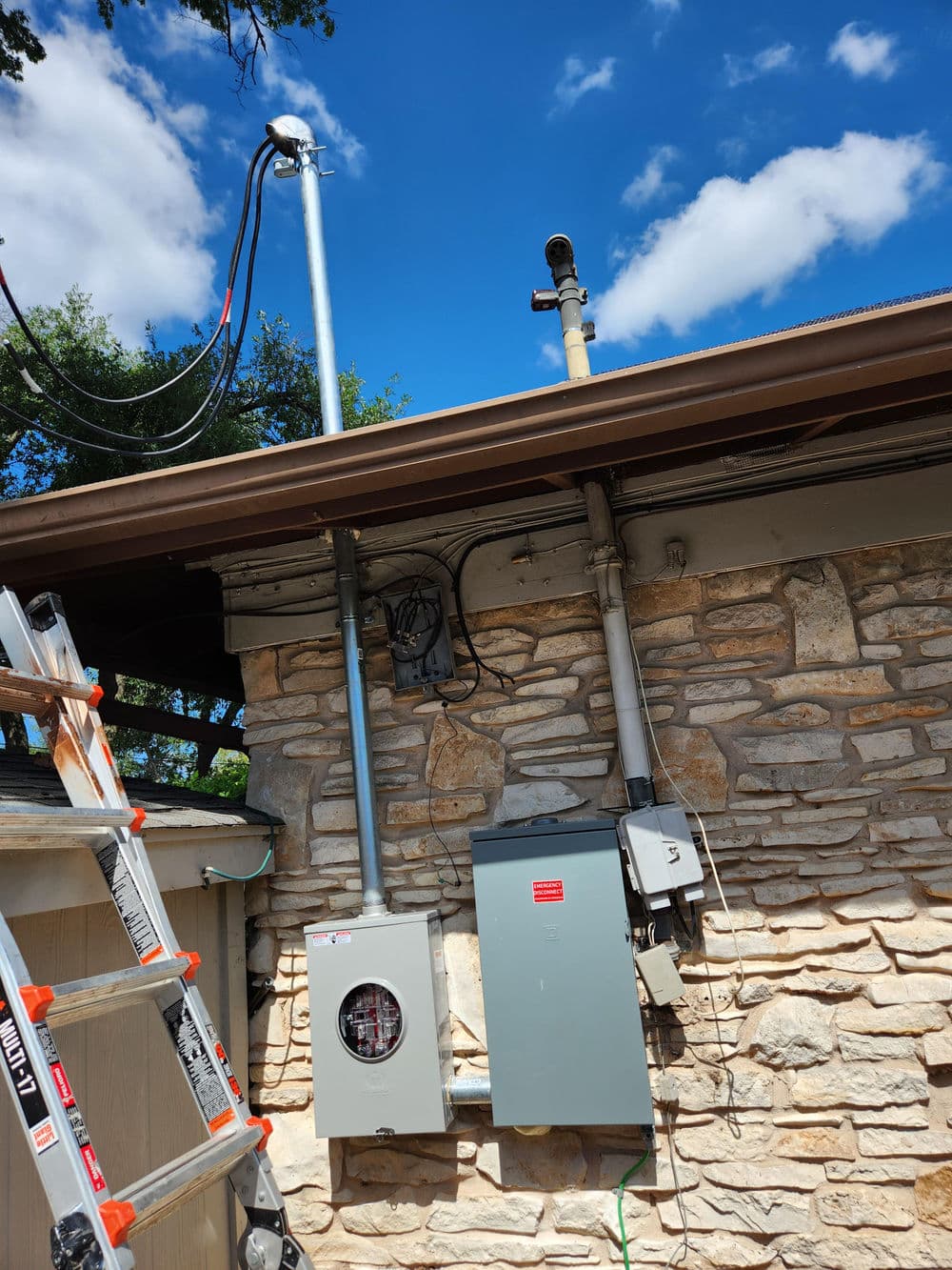 Electrical setup on a building with a ladder, utility boxes, and weather monitoring device.