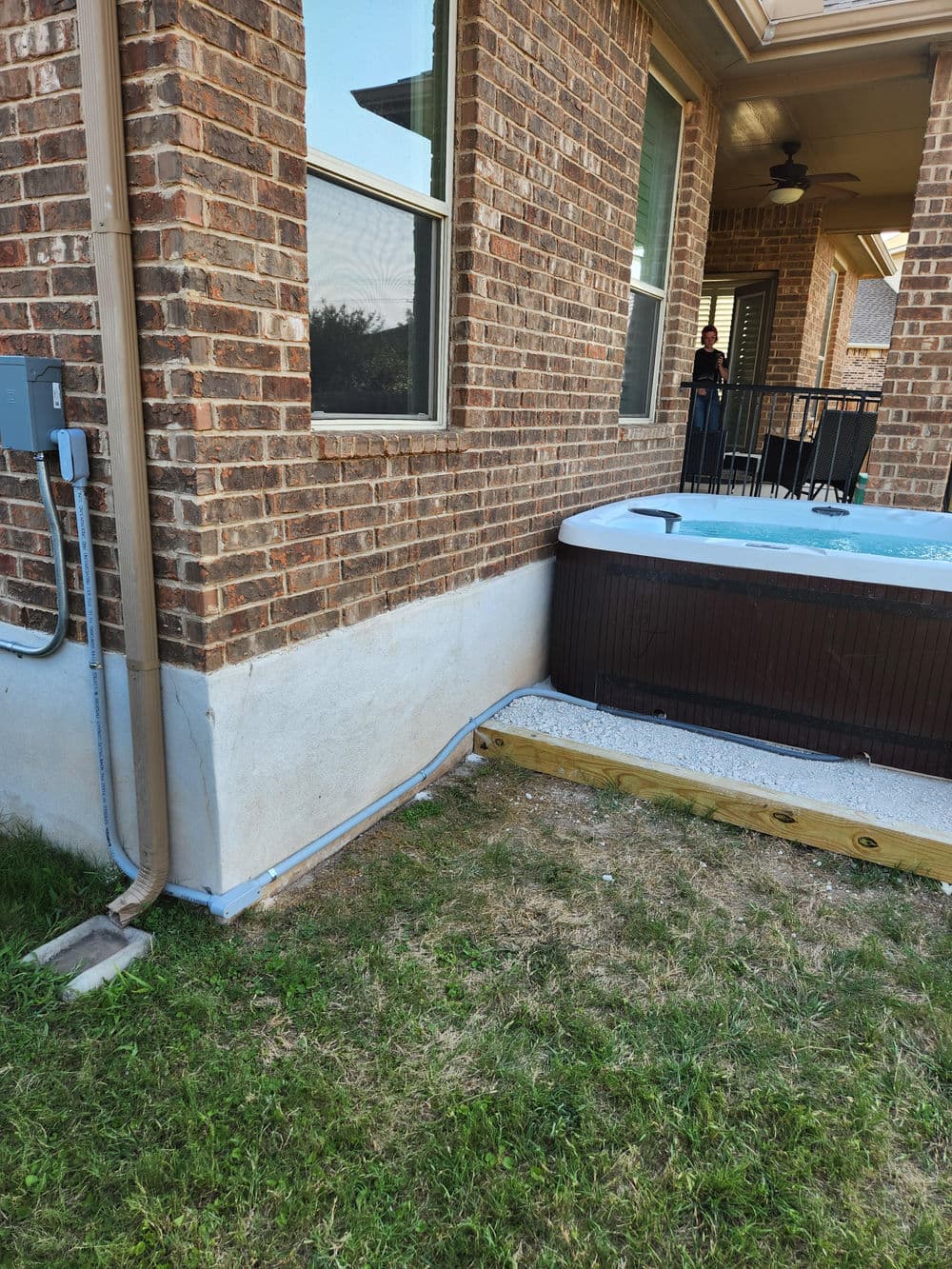 Bricked exterior of a home with a hot tub on a wooden deck and lush green grass.