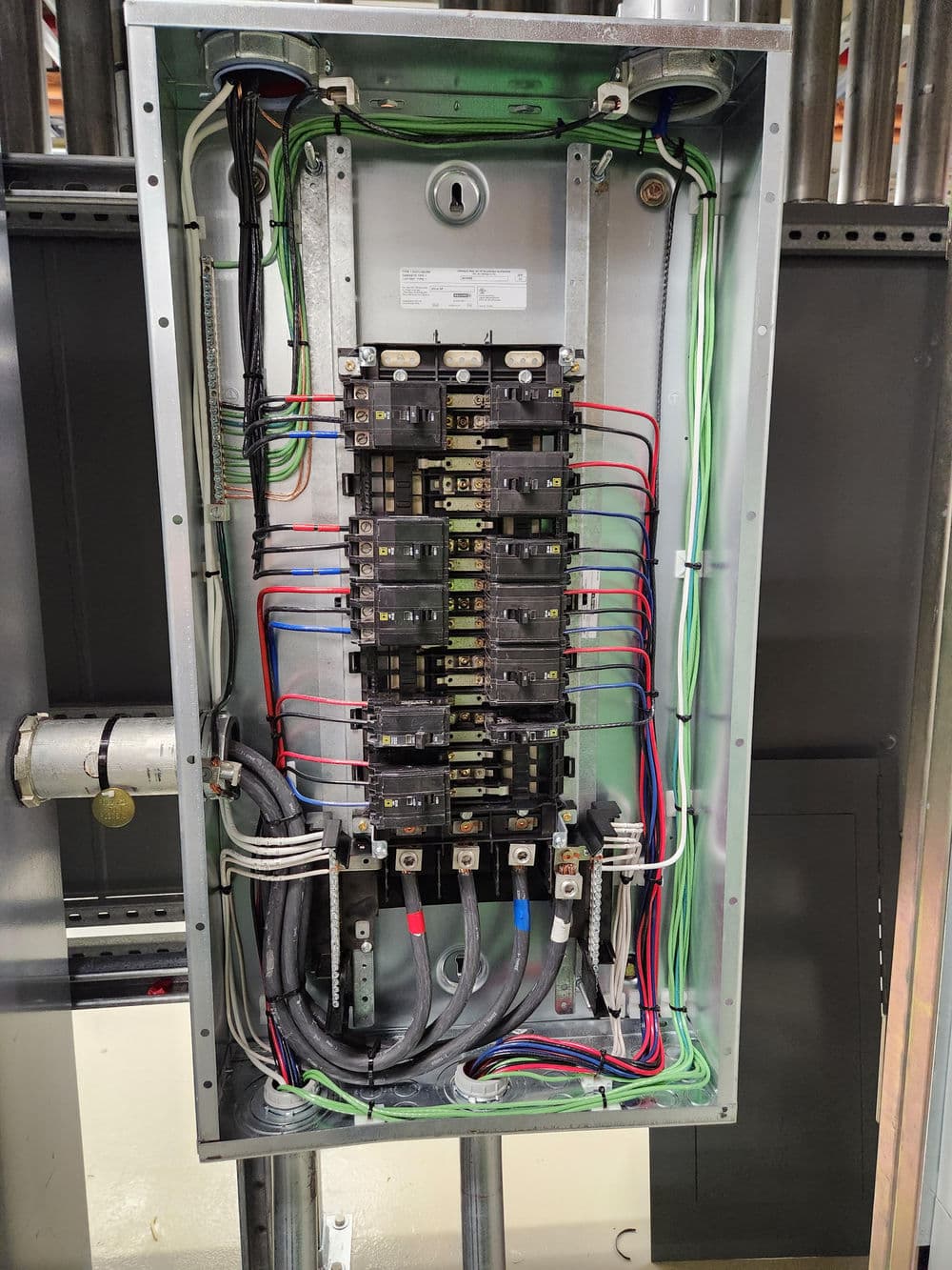 Electrical panel with multiple circuit breakers and wiring connections in a metal enclosure.