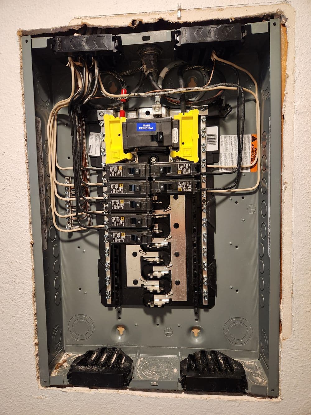 Electrical circuit breaker panel with multiple breakers and wiring connections, mounted on a wall.