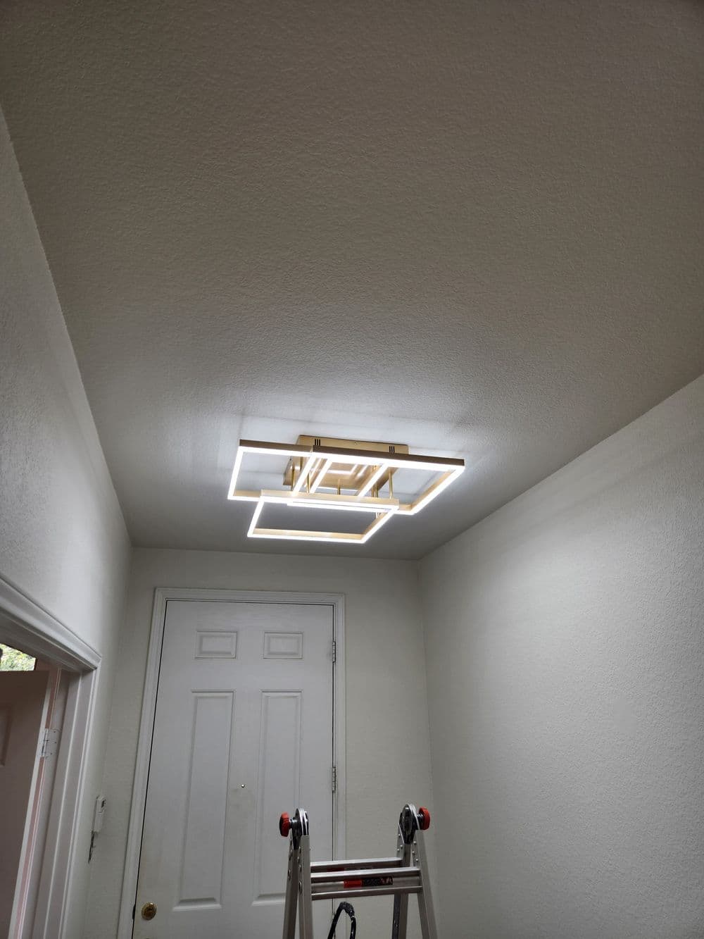 Modern ceiling light fixture installed in a white room with a ladder nearby.