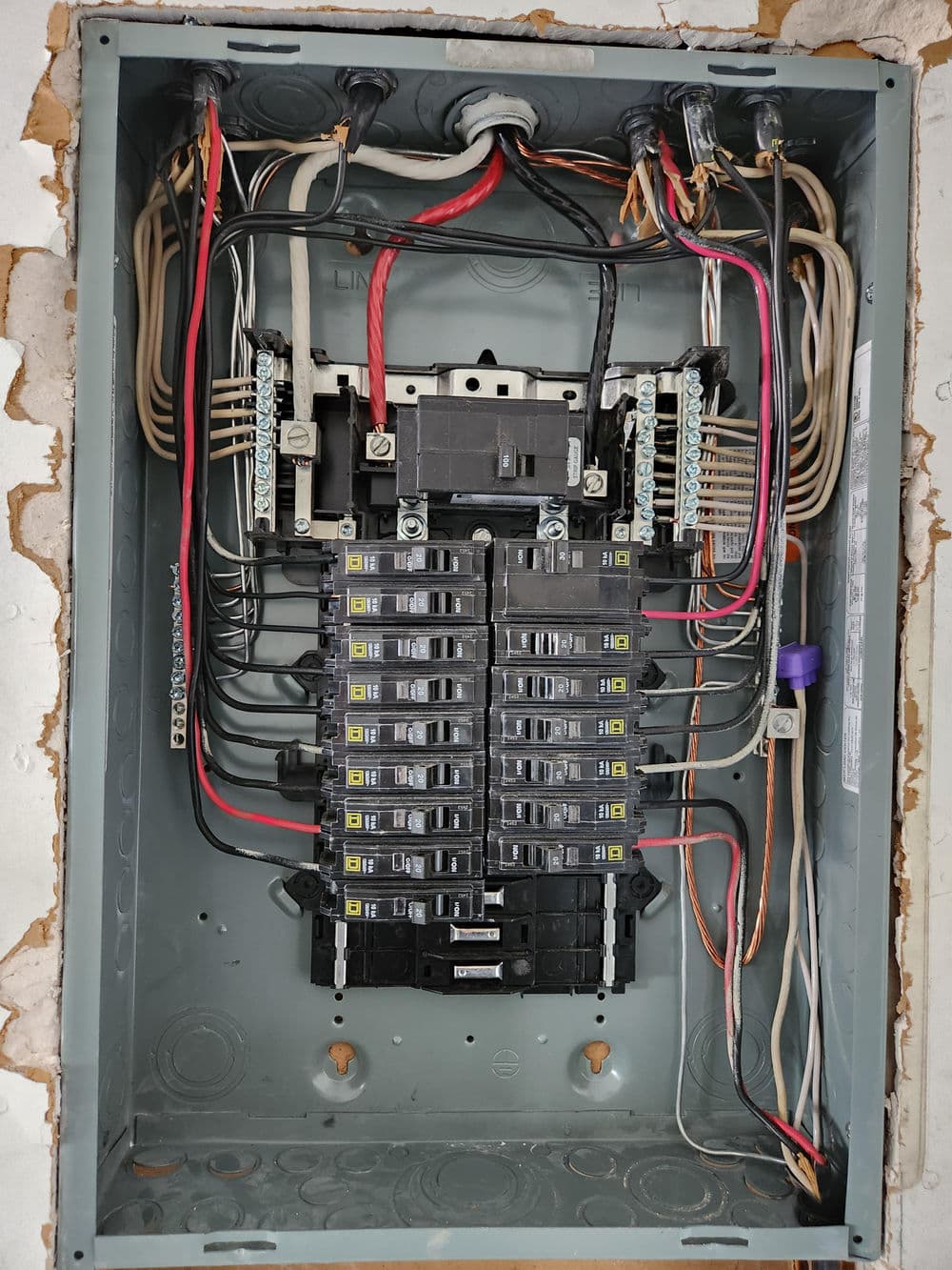 Electrical panel with circuit breakers, wires, and connections in a residential setting.