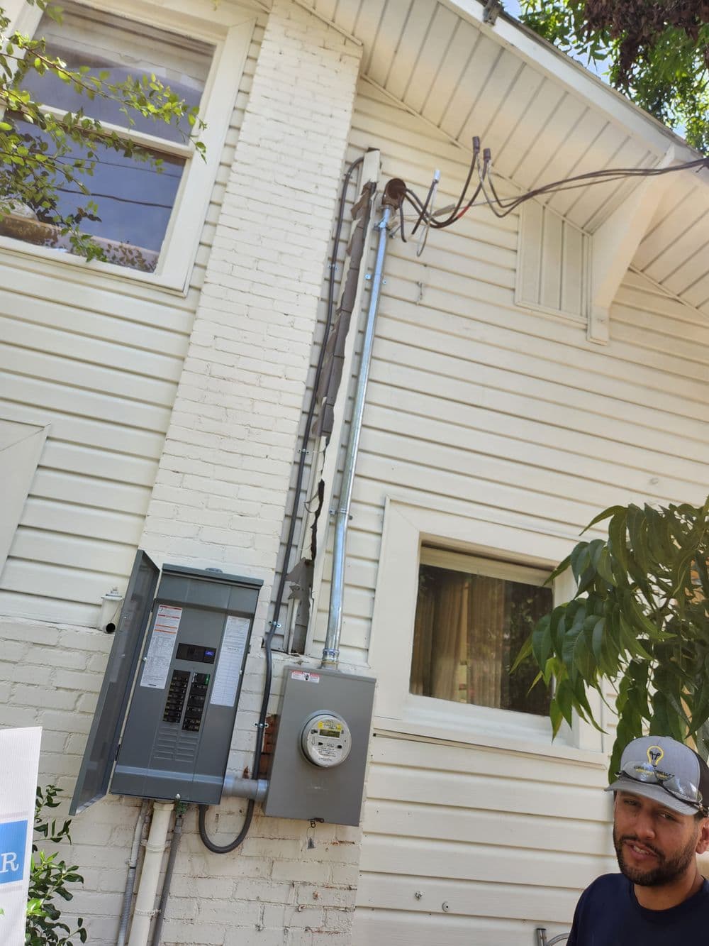 Electric meter and panel on exterior wall with technician inspecting installation.