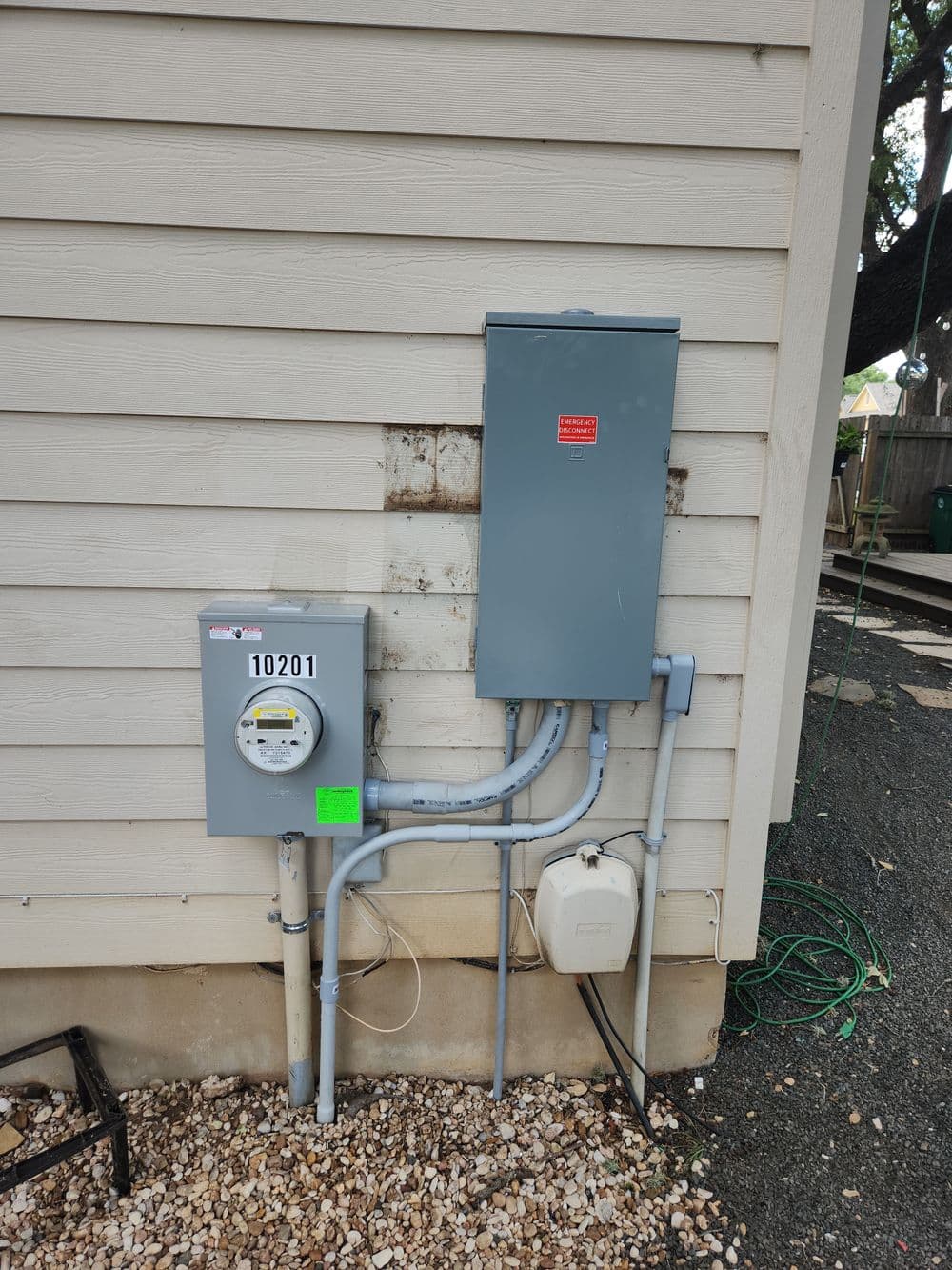 Gray electrical service panel and meter on residential exterior wall with utilities.