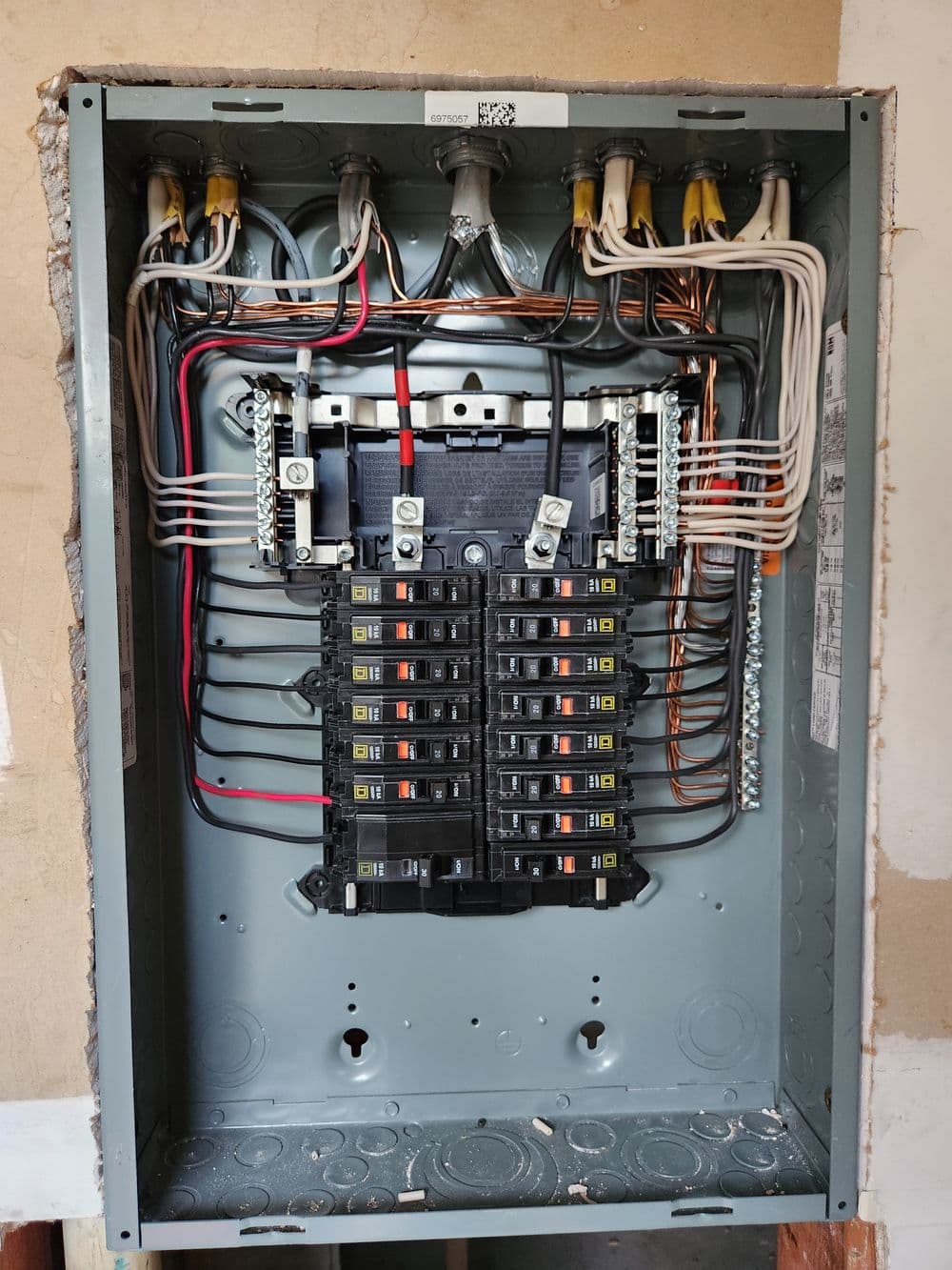 Electrical panel with labeled circuit breakers, wires, and connectors on a wall.
