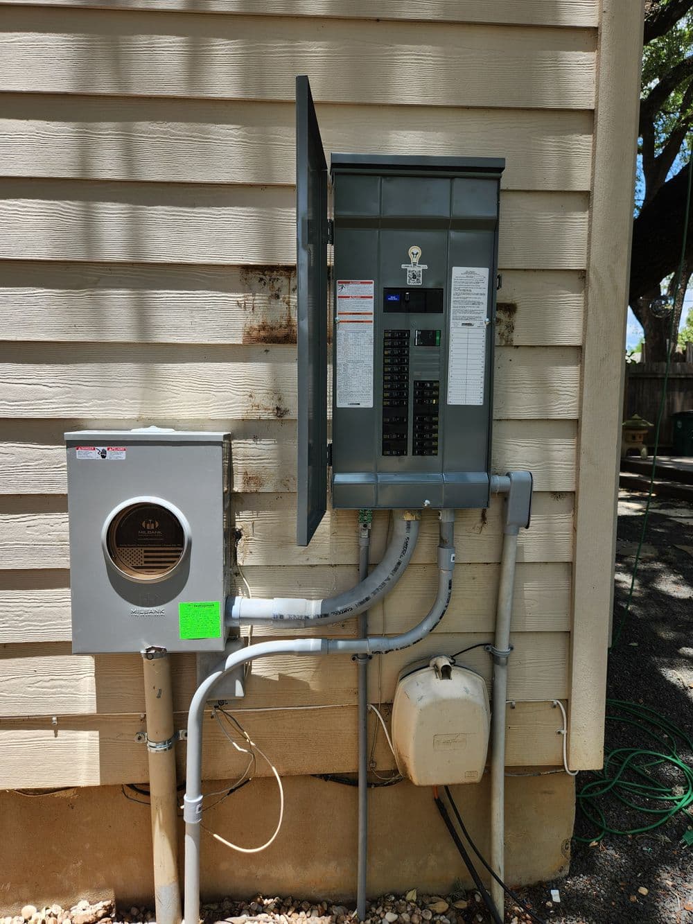 Electrical panel and meter on a house exterior with attached conduit and wiring.