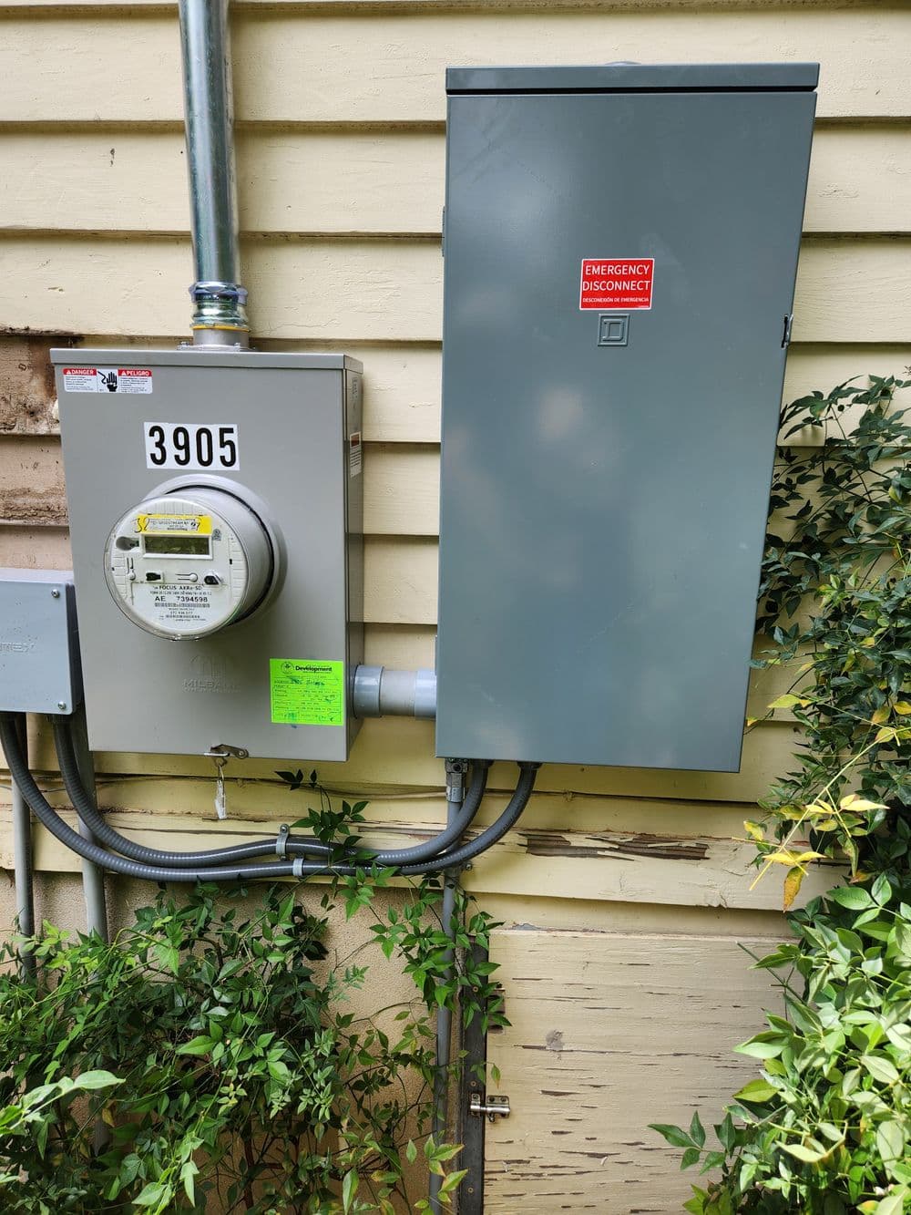 Electrical meter and service panel on exterior wall with emergency disconnect label.