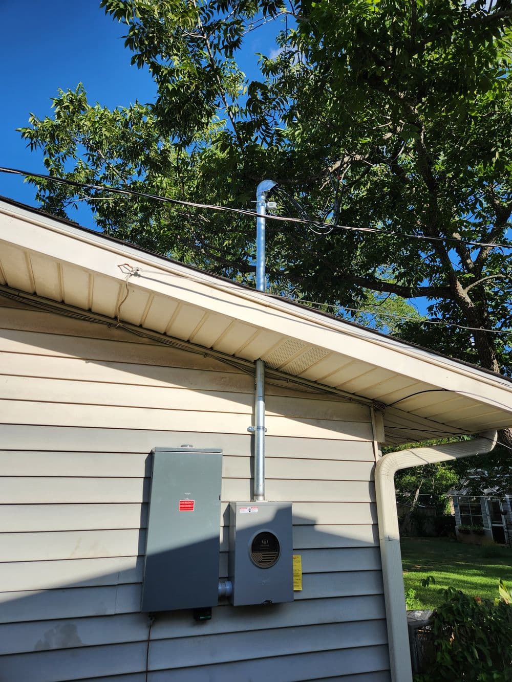 Solar inverter and electrical panel mounted on a house with clear blue sky and trees.