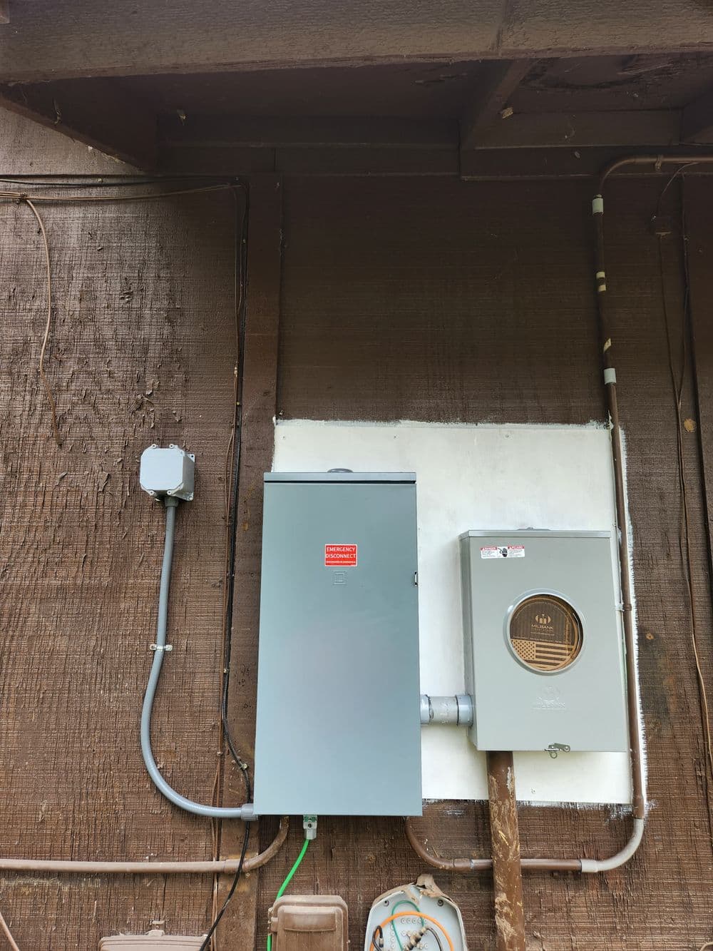 Gray electrical panel and meter on a brown wooden wall. Utility connections visible.