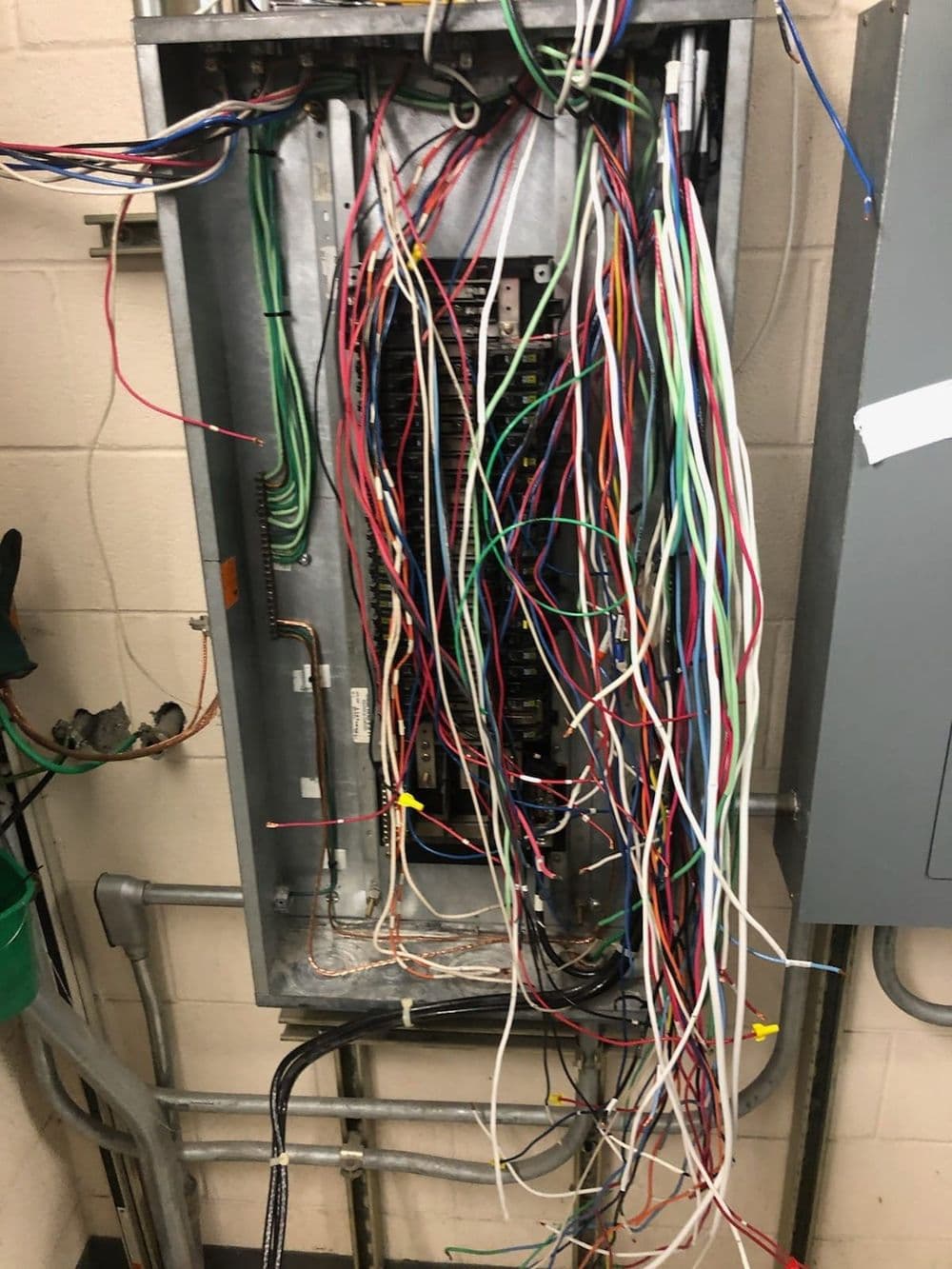 Messy electrical panel with numerous colorful wires tangled inside.
