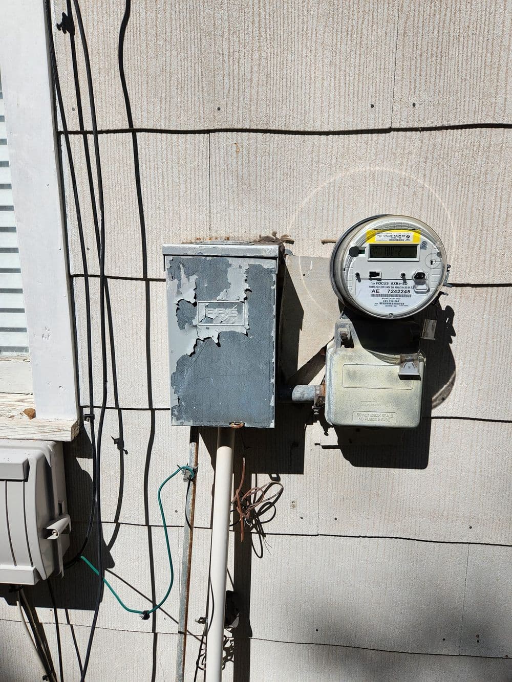 Electric meter and service panel on exterior wall of a house with peeling paint.